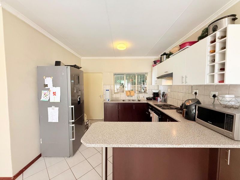 A functional kitchen featuring dark lower cabinetry, white upper cabinets, laminate countertops, a built-in hob, and tiled flooring.