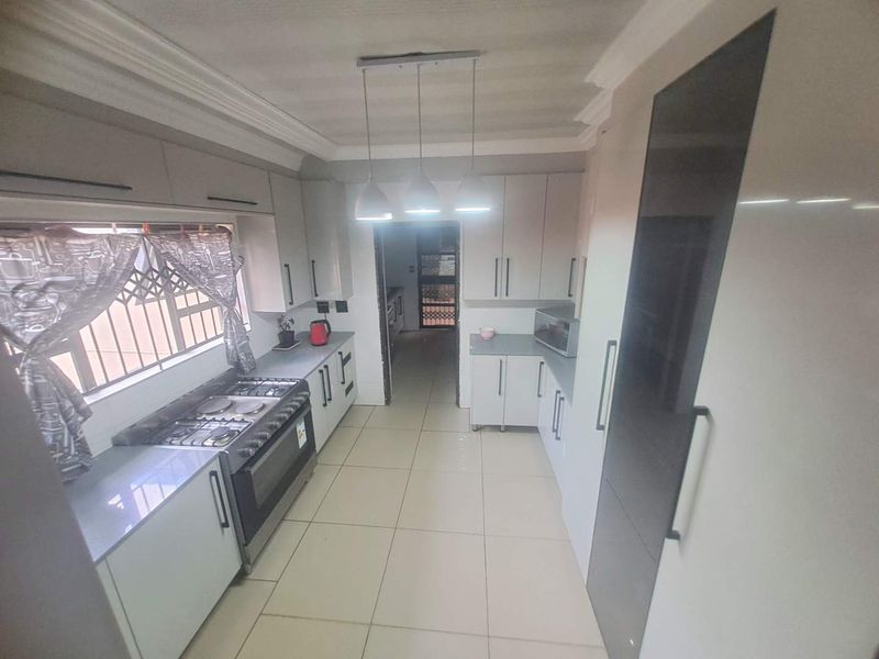 Modern kitchen featuring sleek built-in cabinetry, gas stove, extractor fan, and tiled flooring with direct access to an adjacent utility area.