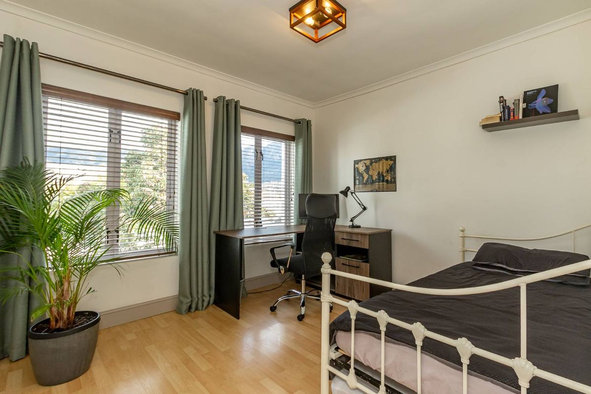 A well-maintained bedroom featuring laminate flooring, neutral walls, and dual windows with venetian blinds and curtain rods, offering a bright and functional living space.