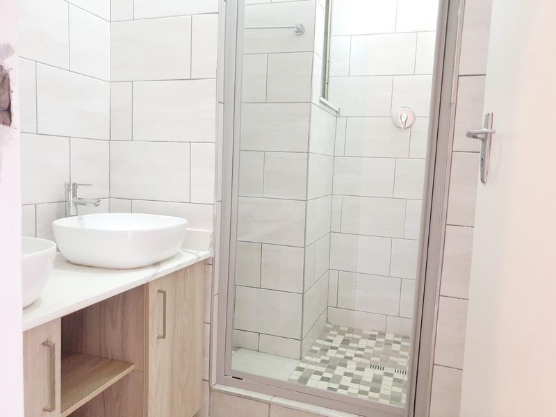 Modern bathroom featuring a vanity with vessel sinks, tiled walls, and a glass-enclosed shower with mosaic floor detailing.