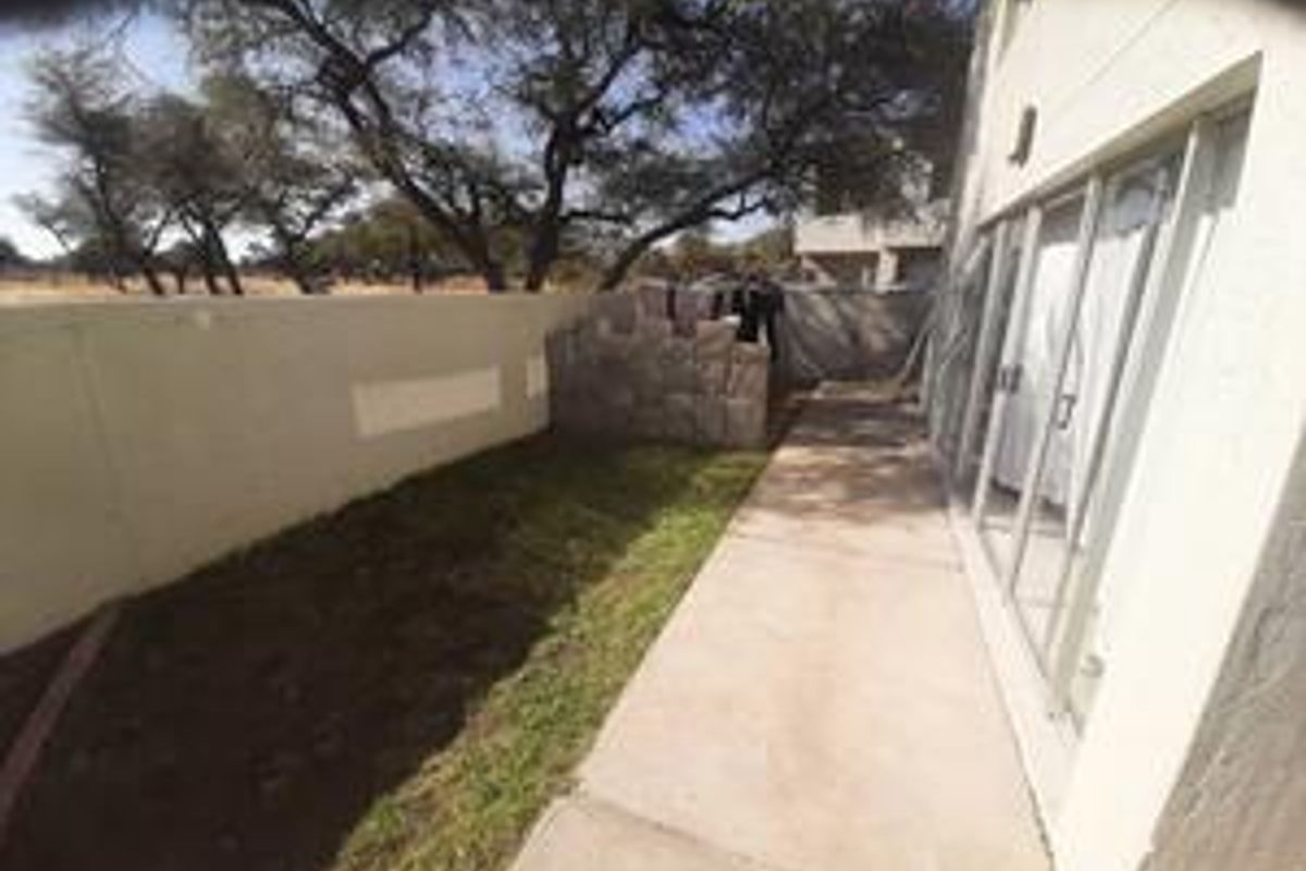 Rear exterior view of the townhouse featuring a concrete patio, sliding glass doors, and a private garden area with boundary walls.