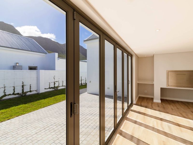 Modern indoor-outdoor entertainment area featuring large aluminium stacker doors, built-in braai, and seamless transition to the paved patio and garden.
