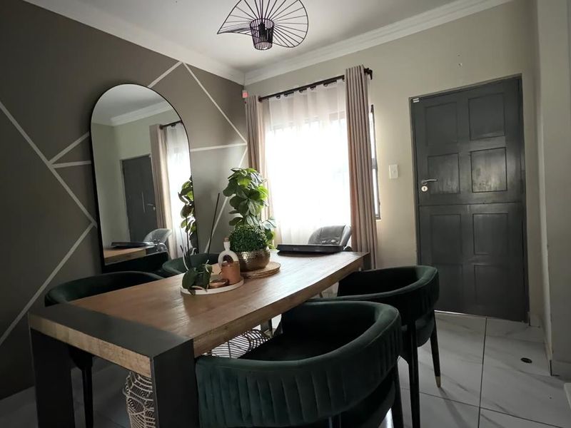 An open-plan dining area featuring tiled flooring, modern geometric wall detailing, and direct access to the kitchen and exterior door.