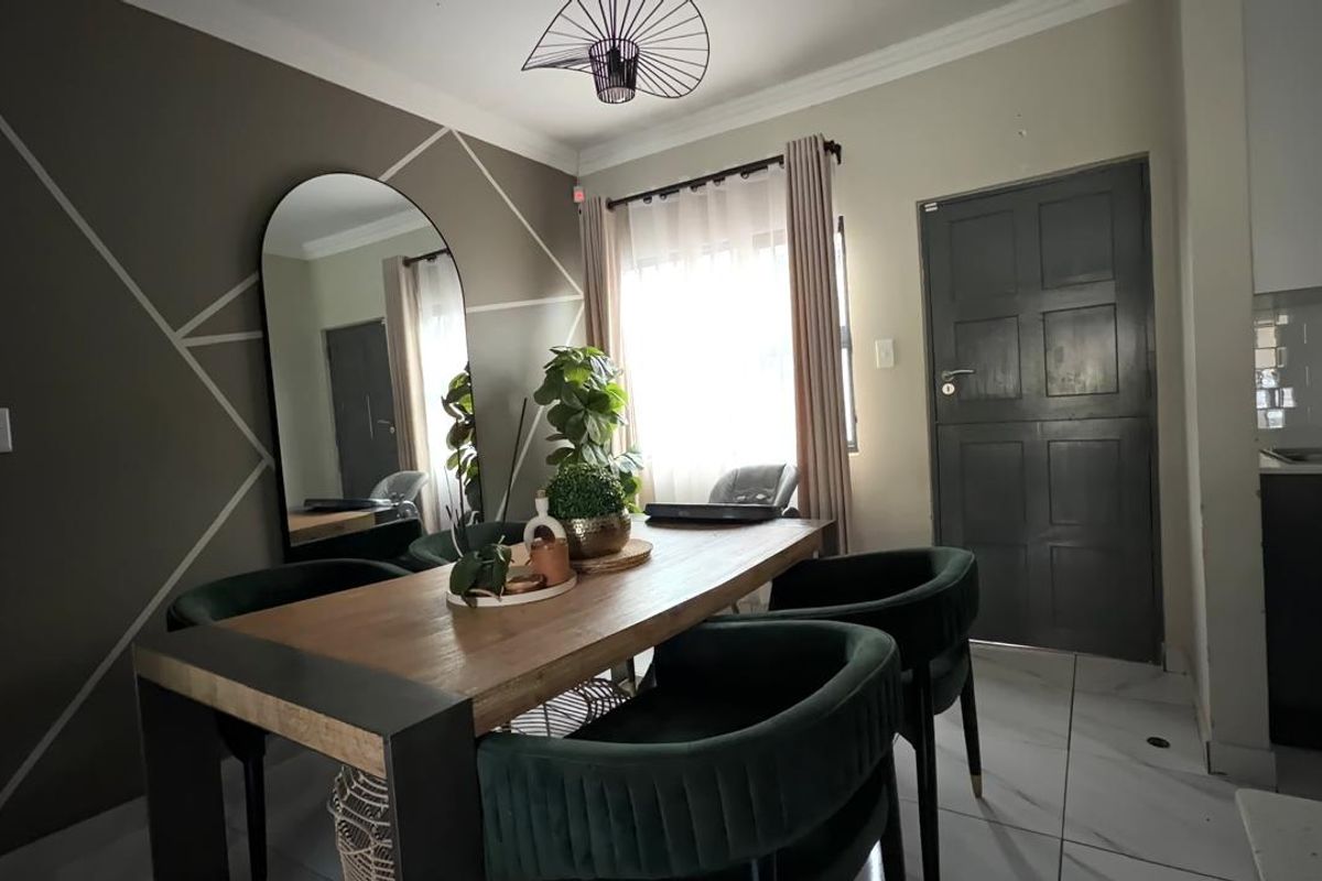 An open-plan dining area featuring tiled flooring, modern geometric wall detailing, and direct access to the kitchen and exterior door.