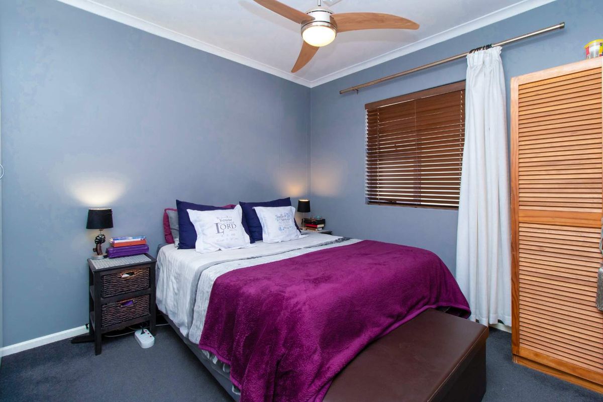 A cozy bedroom featuring blue-toned walls, a ceiling fan, and a built-in wooden wardrobe with louvered doors.