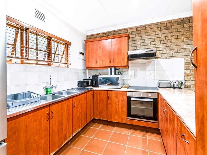 Functional kitchen featuring wooden cabinetry, laminate countertops, built-in oven, electric hob, and a distinctive exposed brick feature wall.