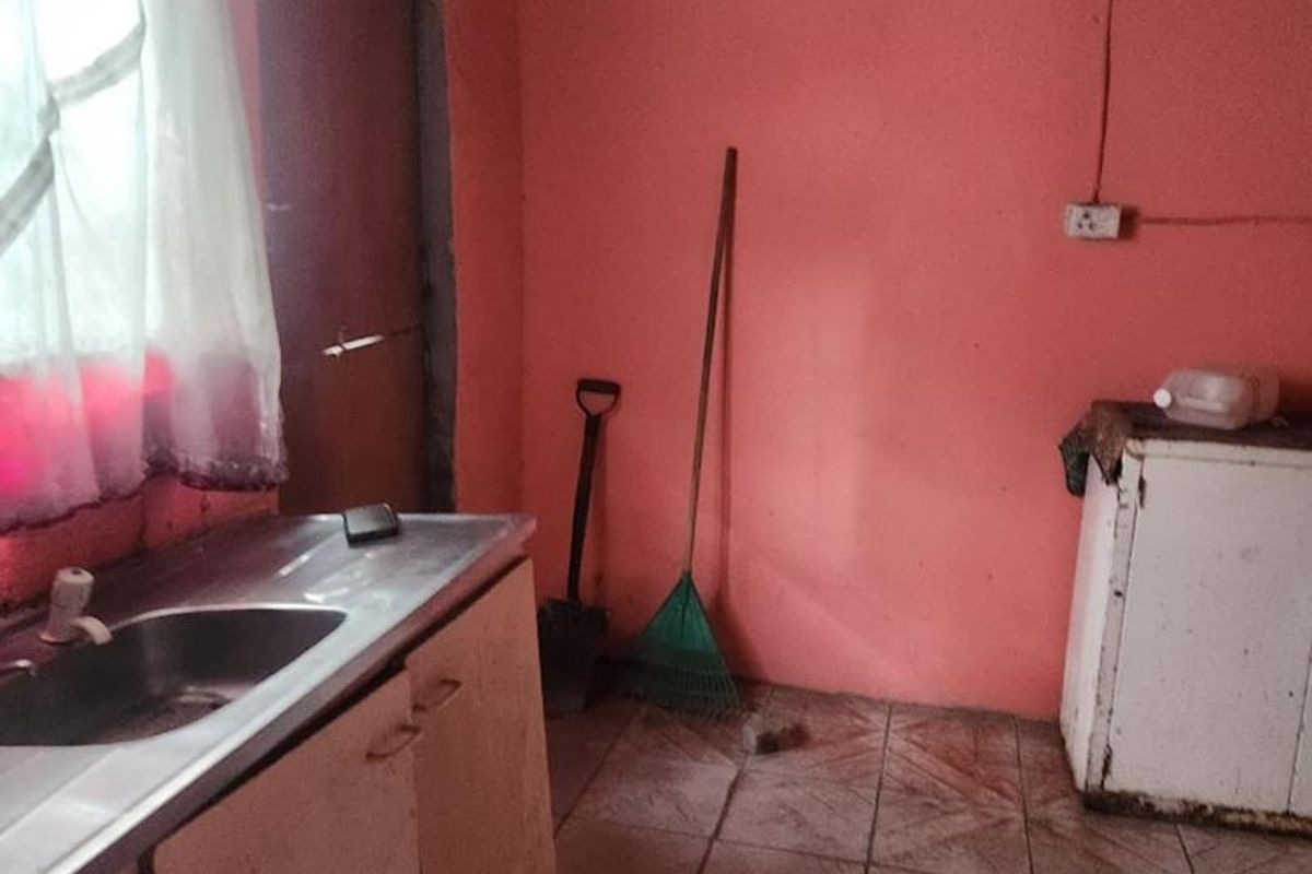 A dated kitchen area featuring a stainless steel sink, tiled flooring, and timber ceiling, requiring significant renovation and cosmetic updates.
