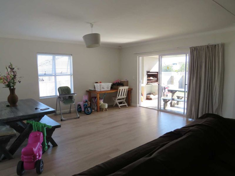 Spacious living area featuring light laminate flooring and large sliding glass doors that provide seamless access to the outdoor patio and built-in braai area.
