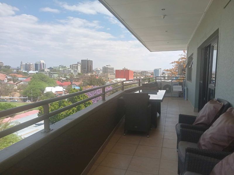 A spacious covered balcony featuring tiled flooring and a metal balustrade, offering expansive city views.