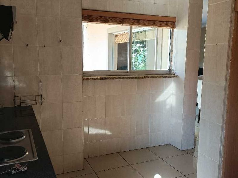 A functional kitchen area featuring granite countertops, a built-in electric hob, and neutral ceramic tiling throughout, offering a clean and practical workspace.