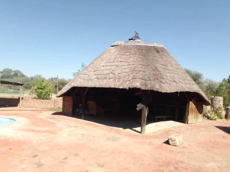 An open-air thatched lapa area featuring brick paving and timber support posts, situated adjacent to the pool area on the small holding.
