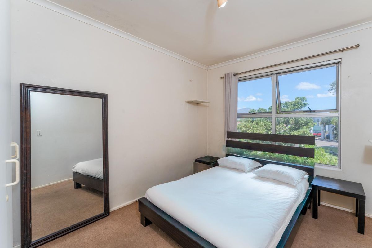 A functional bedroom featuring a large window with natural light, neutral wall finishes, and carpeted flooring.