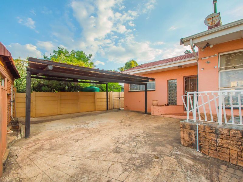 Rear exterior view featuring a concrete driveway, a covered carport, and a stone-clad patio area with security features.