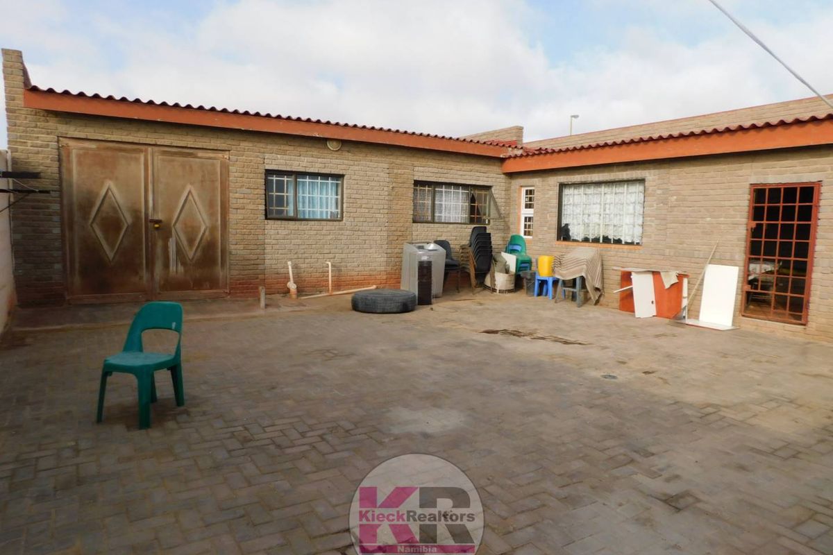 Rear exterior view of the property featuring a paved courtyard, face brick facade, and secure metal door access.