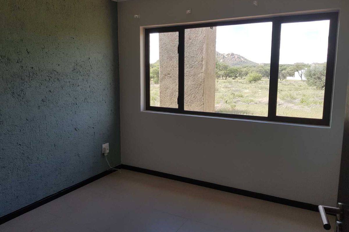 An empty bedroom featuring tiled flooring, a textured accent wall, and large windows offering natural light and scenic landscape views.
