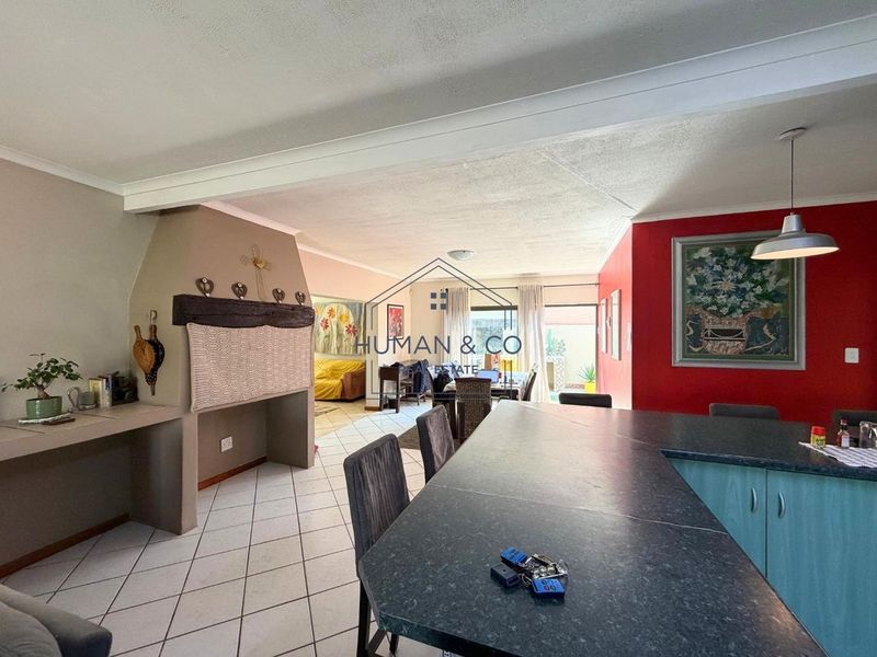 Open-plan living and kitchen area featuring a built-in fireplace, tiled flooring, and a central kitchen island with direct access to the outdoor patio.