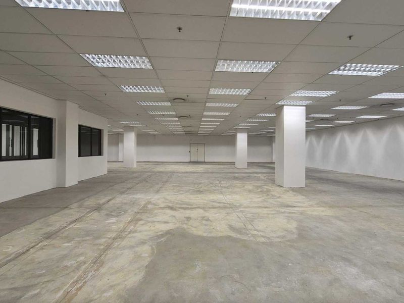 A large, open-plan commercial retail space featuring a suspended ceiling, recessed lighting, structural columns, and unfinished concrete flooring.