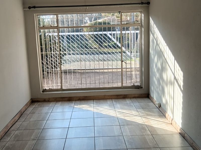 An empty living room featuring tiled flooring, large windows with security bars, and natural light, offering a blank canvas for interior design.