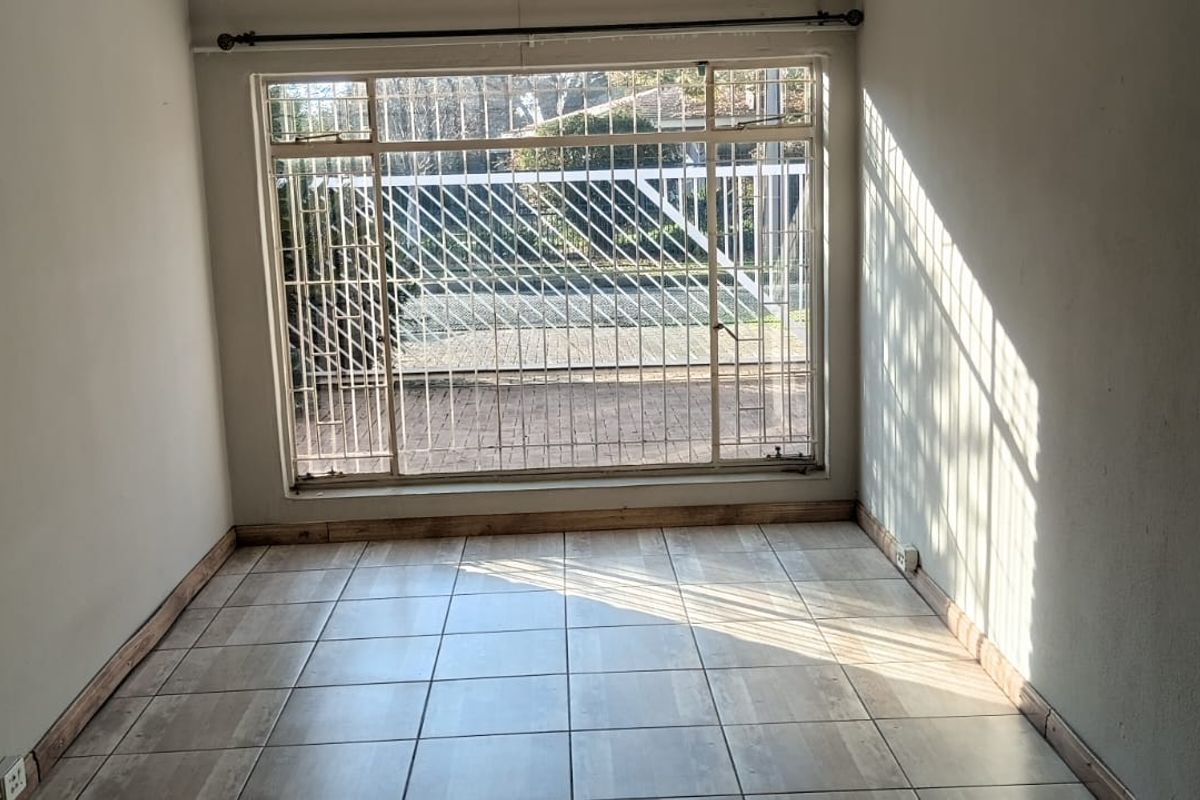 An empty living room featuring tiled flooring, large windows with security bars, and natural light, offering a blank canvas for interior design.