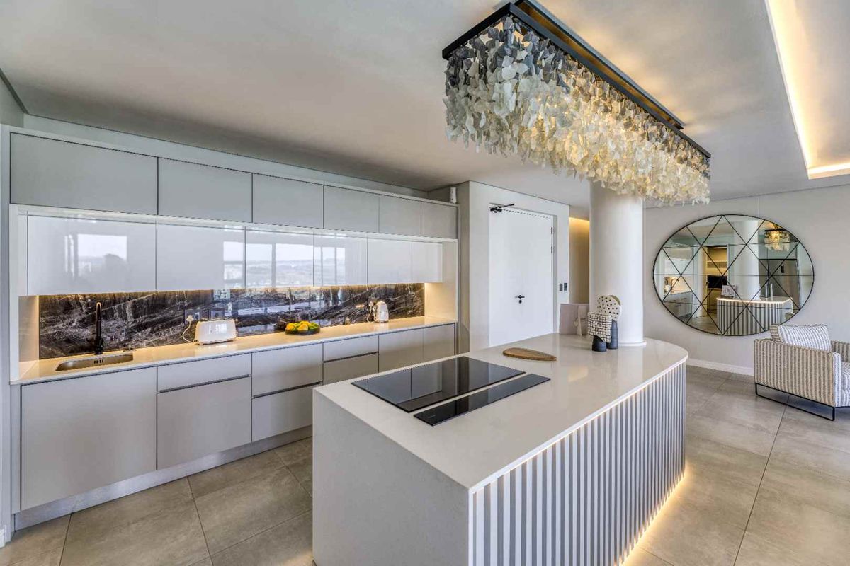 Modern open-plan kitchen featuring a large central island with integrated hob, sleek cabinetry, stone backsplash, and sophisticated recessed and pendant lighting.