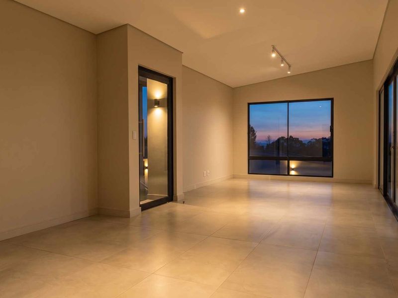 A spacious, modern, and empty living area featuring large format floor tiles, recessed lighting, and expansive windows with views.