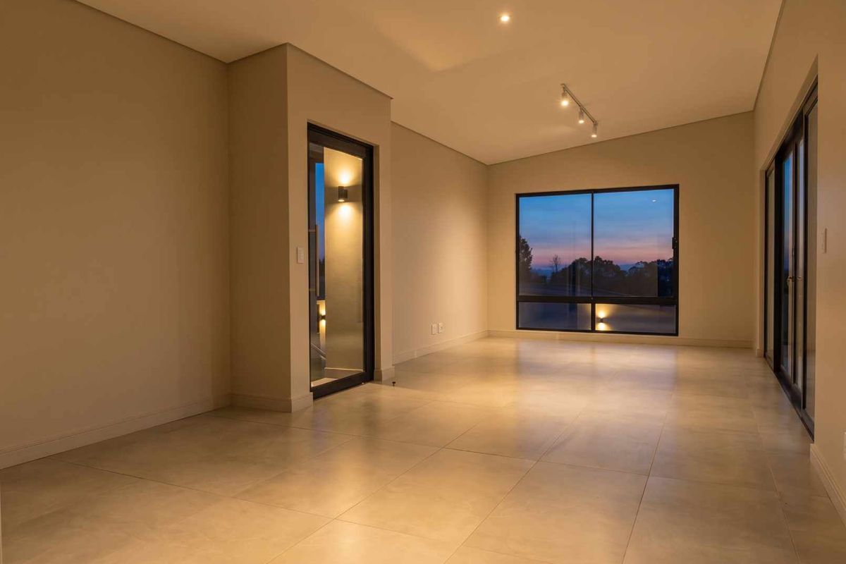 A spacious, modern, and empty living area featuring large format floor tiles, recessed lighting, and expansive windows with views.