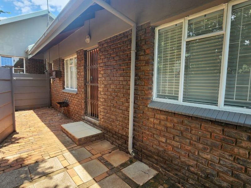 A rear exterior view of the cottage featuring a face brick facade, paved patio area, and secure entrance with a metal security gate.