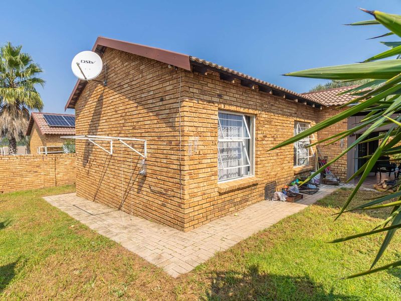 Rear view of a face-brick townhouse featuring a tiled roof, paved walkway, and established garden area.