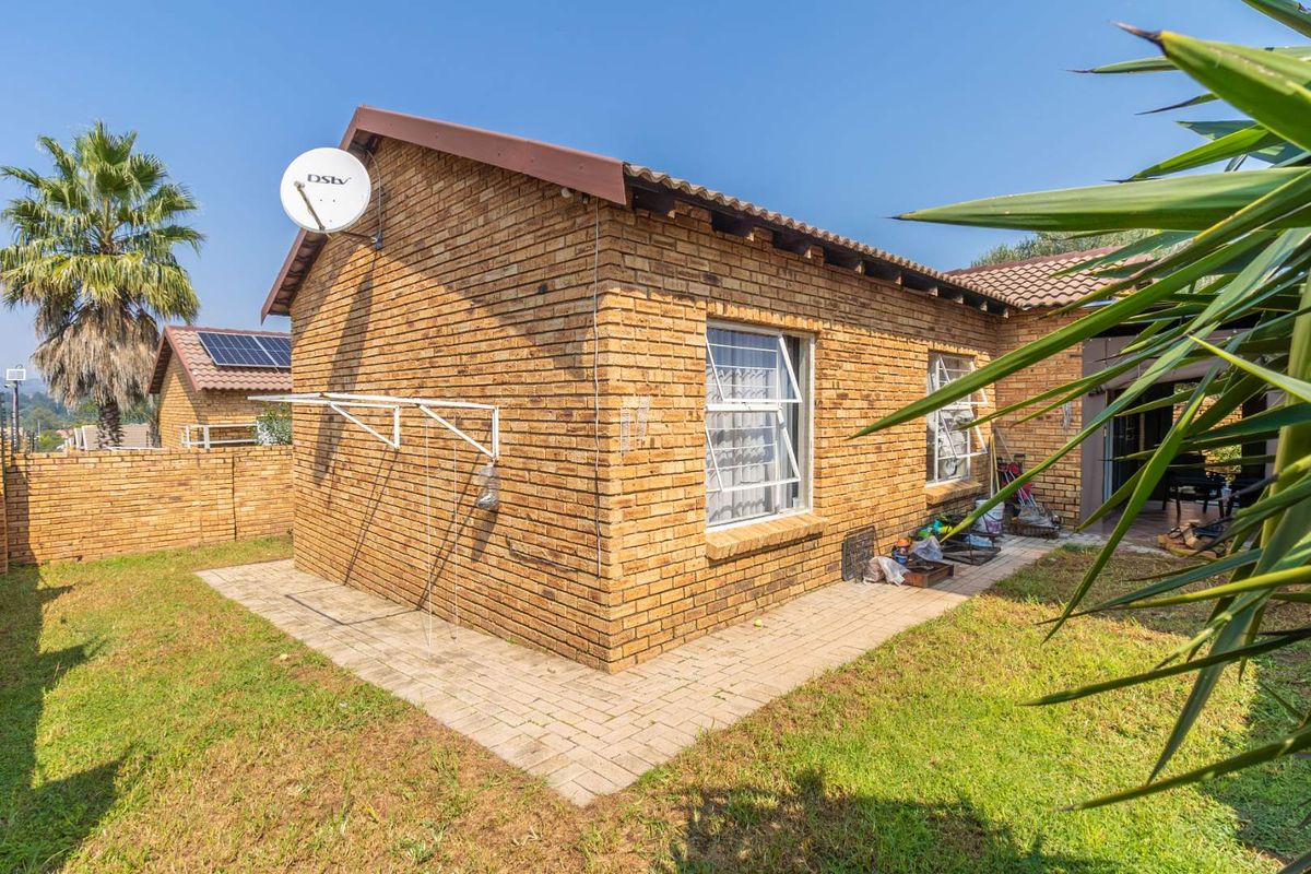 Rear view of a face-brick townhouse featuring a tiled roof, paved walkway, and established garden area.