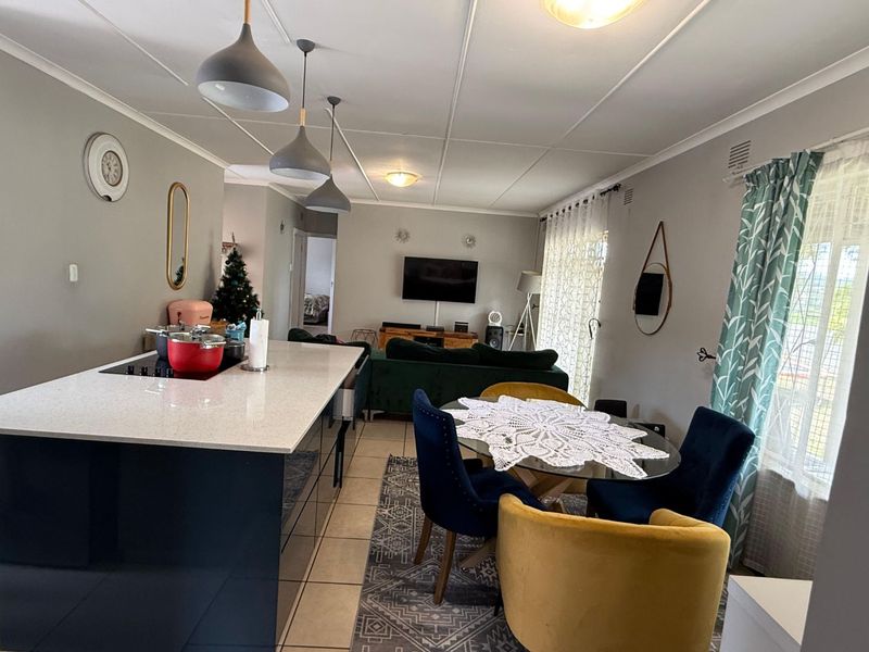 Spacious open-plan living area featuring a modern kitchen island with stone countertops, integrated hob, and contemporary pendant lighting, seamlessly connecting to the dining space.