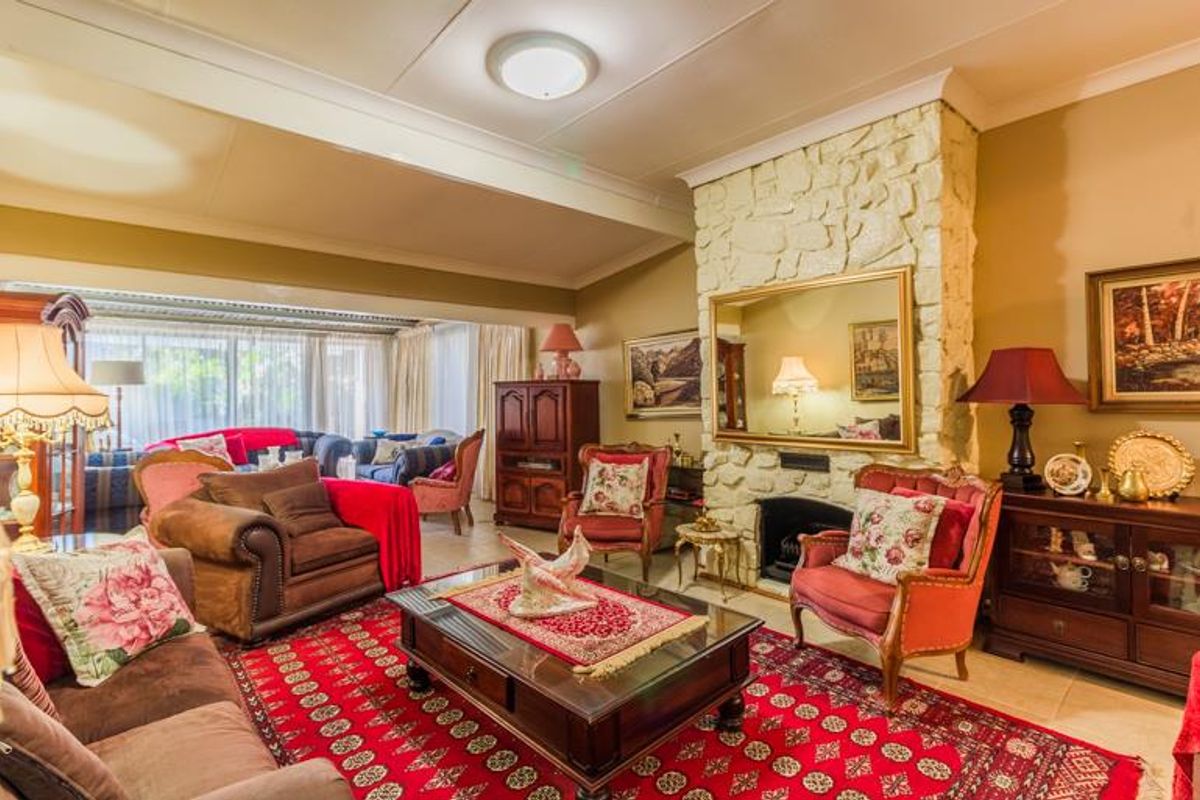 A traditional living room featuring a prominent stone-clad fireplace, tiled flooring, and a spacious layout with access to an adjoining sunroom area.