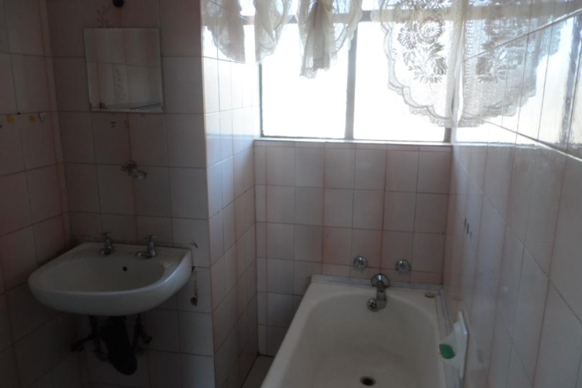 A dated bathroom featuring a wall-mounted basin and a built-in bathtub with full-height ceramic wall tiling.