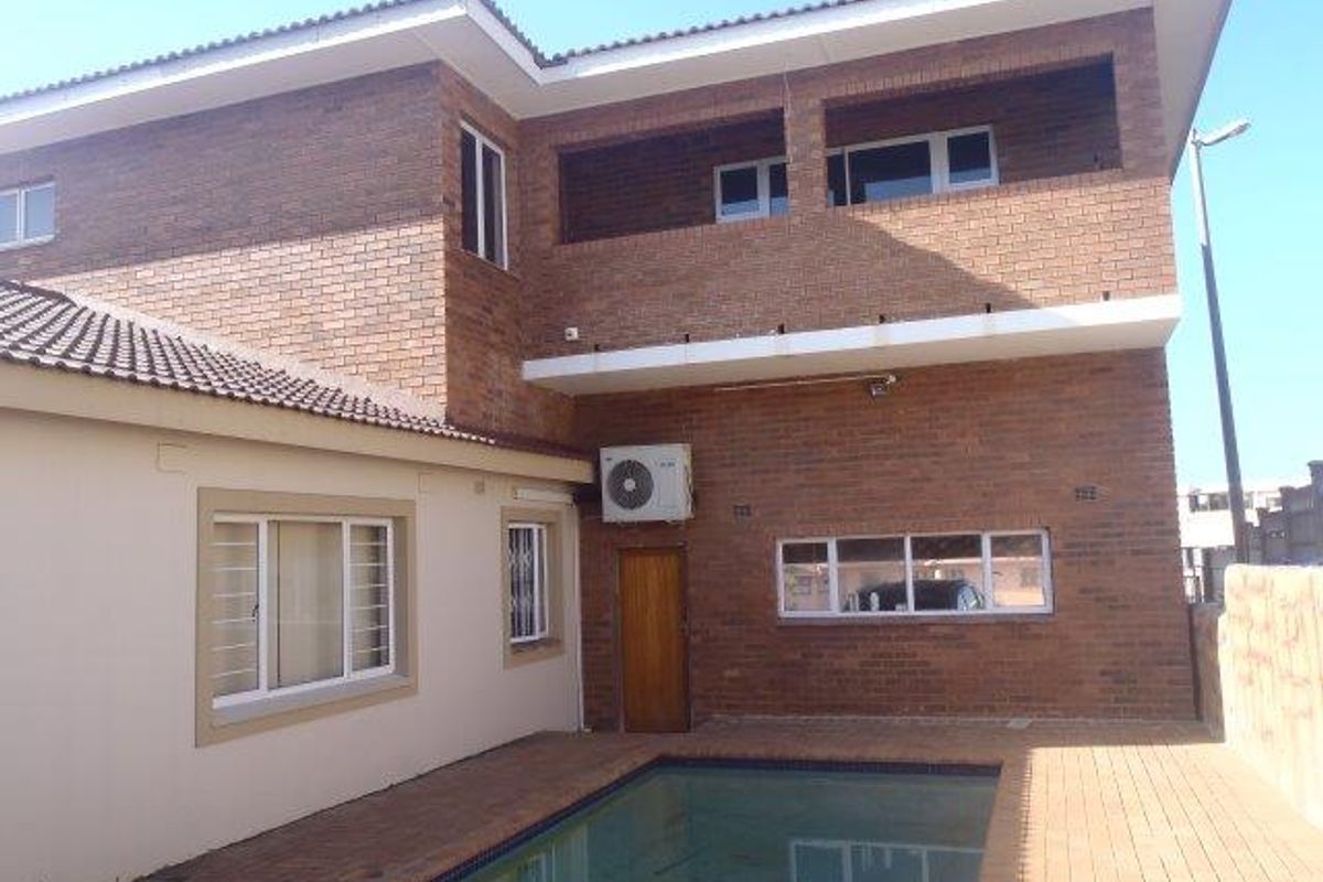 Rear exterior view of a two-story brick house featuring a swimming pool, paved patio area, and an upper-level balcony.