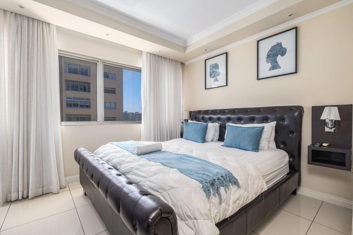 A well-maintained bedroom featuring tiled flooring, recessed ceiling lighting, and large windows that provide natural light and urban views.