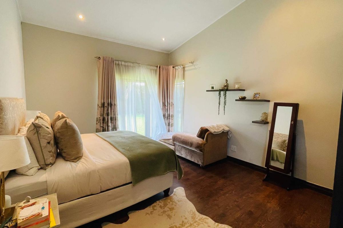 A well-maintained bedroom featuring dark wood flooring, recessed ceiling lighting, and large windows with curtains providing natural light and garden access.