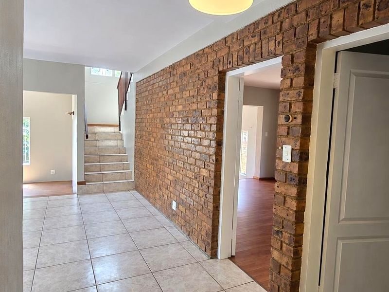 A spacious hallway featuring exposed brickwork, tiled flooring, and a staircase leading to the upper level, providing access to multiple rooms.