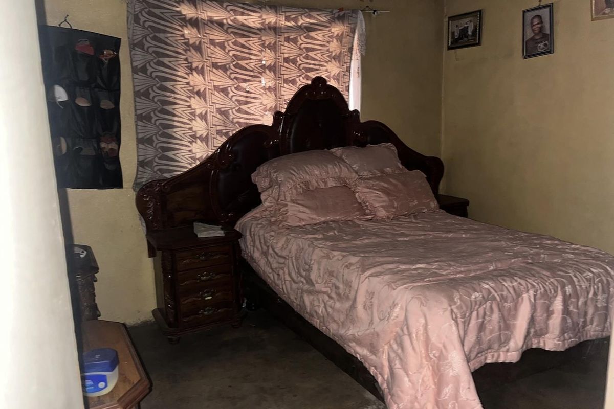 A bedroom featuring basic wall finishes and a window with a ventilation grille, requiring cosmetic updates to improve the overall aesthetic.