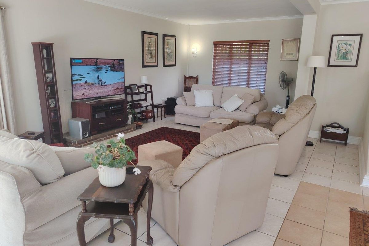 A spacious living room featuring neutral wall tones, tiled flooring, and natural light filtered through venetian blinds, offering a comfortable and functional living space.