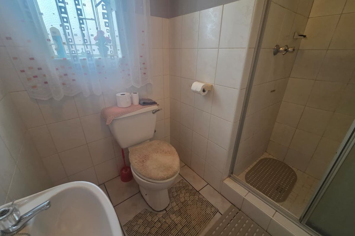A functional bathroom featuring a shower enclosure, toilet, and pedestal basin with tiled walls and flooring.