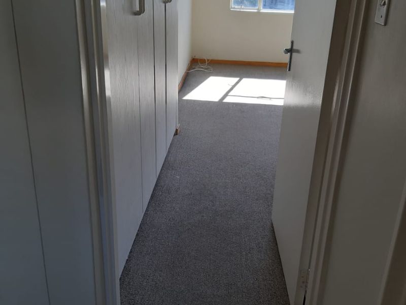 An empty bedroom featuring built-in cupboards, carpeted flooring, and a window allowing natural light.