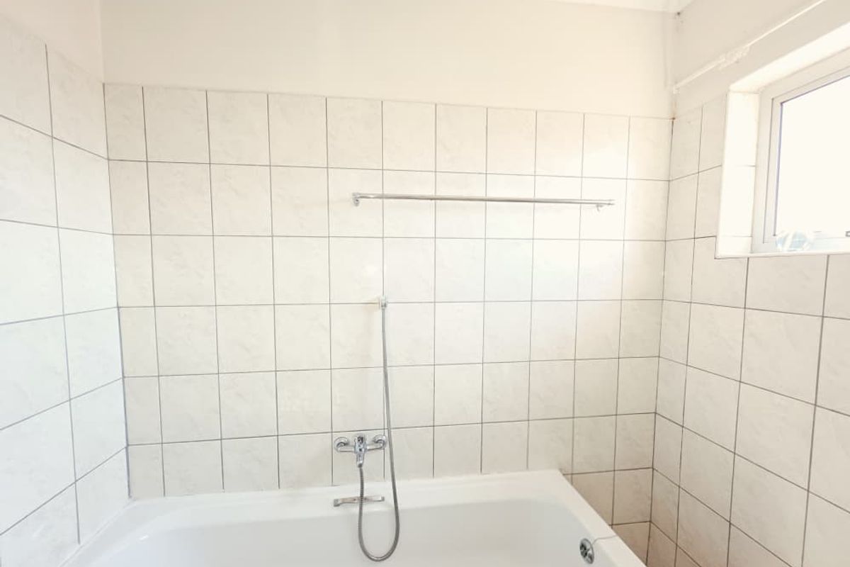 A functional bathroom featuring a bathtub with a shower mixer, tiled walls, and a window, requiring some cosmetic updates to the ceiling and grout.