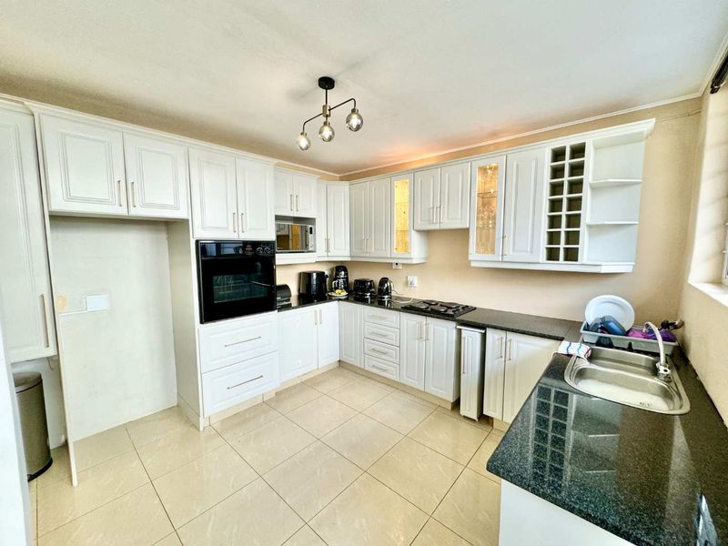 A functional kitchen featuring white shaker-style cabinetry, dark granite countertops, built-in oven, gas hob, and tiled flooring.