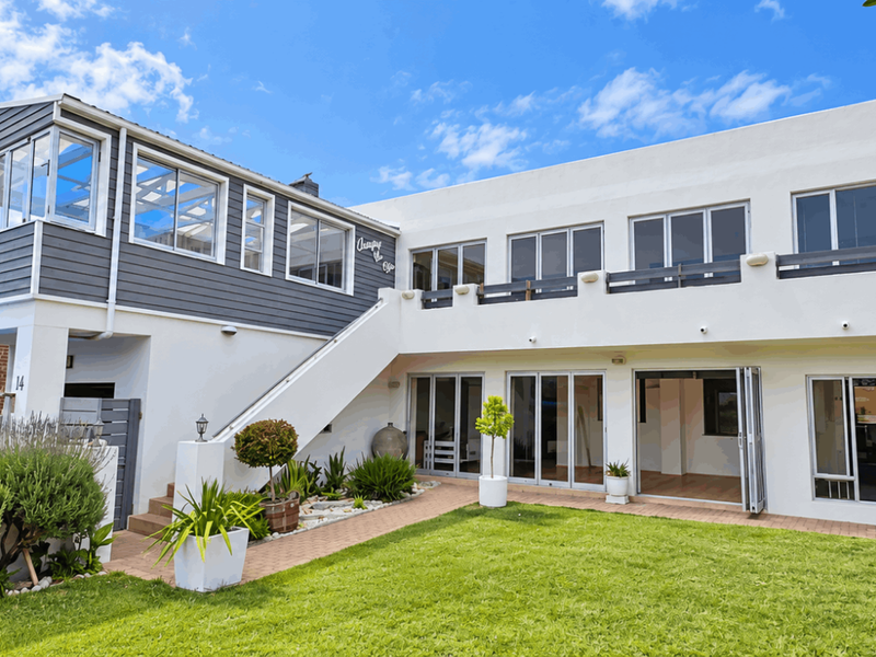 Rear view of a two-story house featuring a landscaped garden, paved walkway, balcony, and large bi-fold doors providing seamless indoor-outdoor flow.
