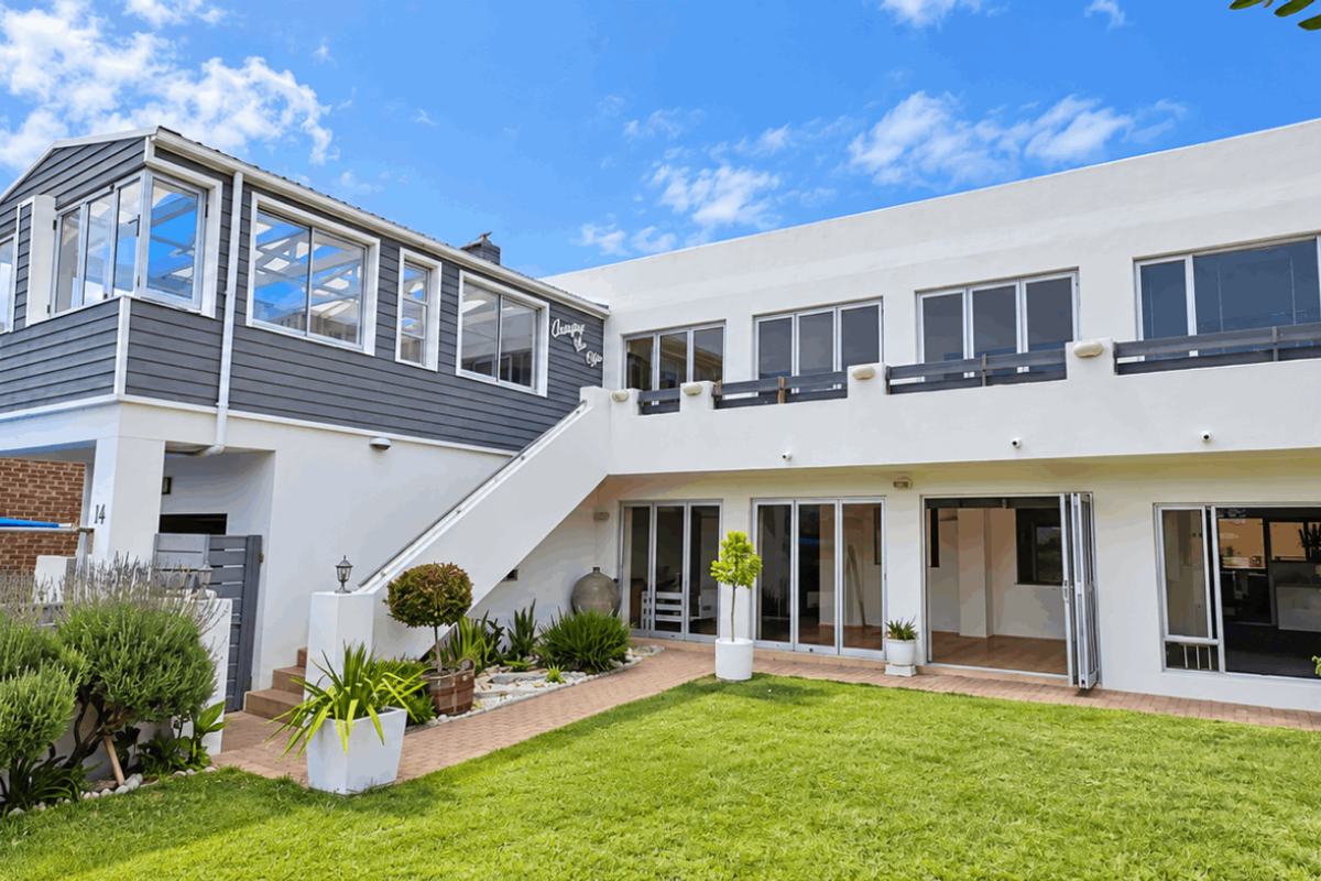 Rear view of a two-story house featuring a landscaped garden, paved walkway, balcony, and large bi-fold doors providing seamless indoor-outdoor flow.