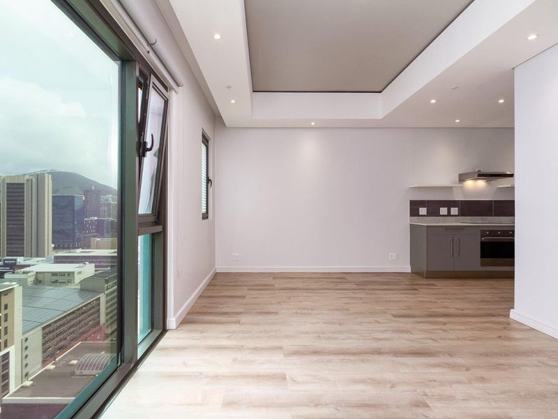 Modern open-plan living area featuring laminate flooring, recessed ceiling lighting, and a sleek kitchen with built-in appliances, complemented by expansive city views.