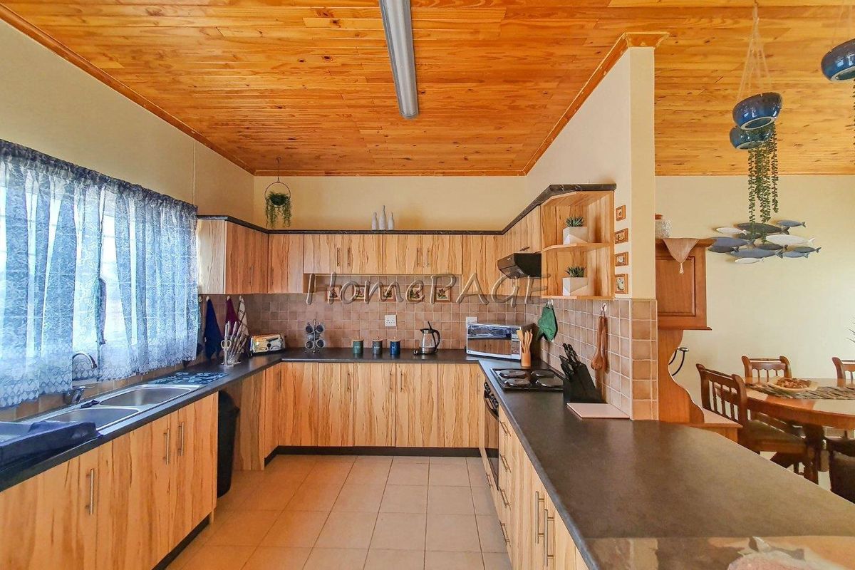 A functional kitchen featuring wood-grain cabinetry, dark countertops, tiled splashbacks, and a timber-paneled ceiling, offering a warm and traditional aesthetic.
