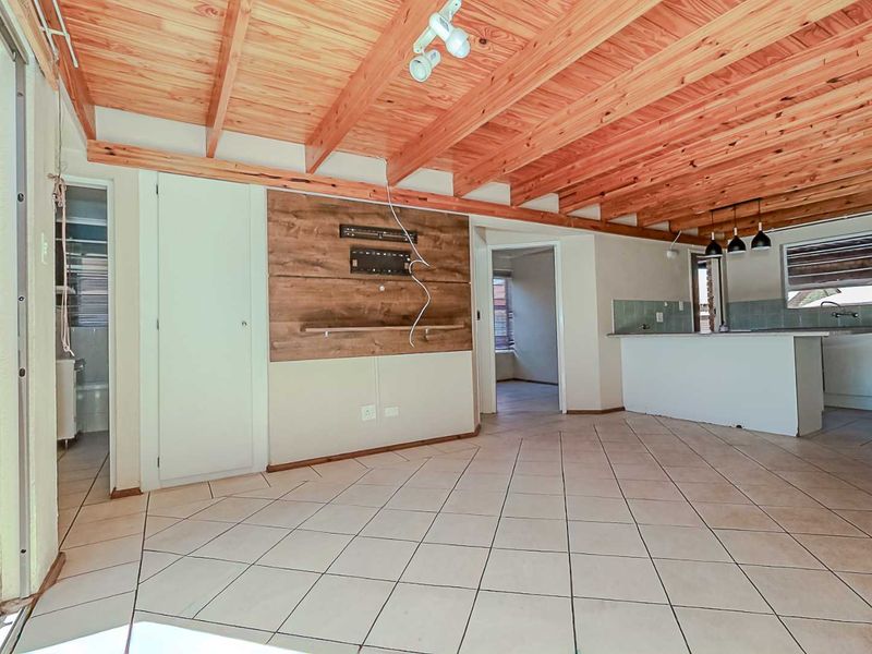 Spacious open-plan living and kitchen area featuring exposed timber beam ceilings, tiled flooring, and a functional kitchen island with built-in cabinetry.