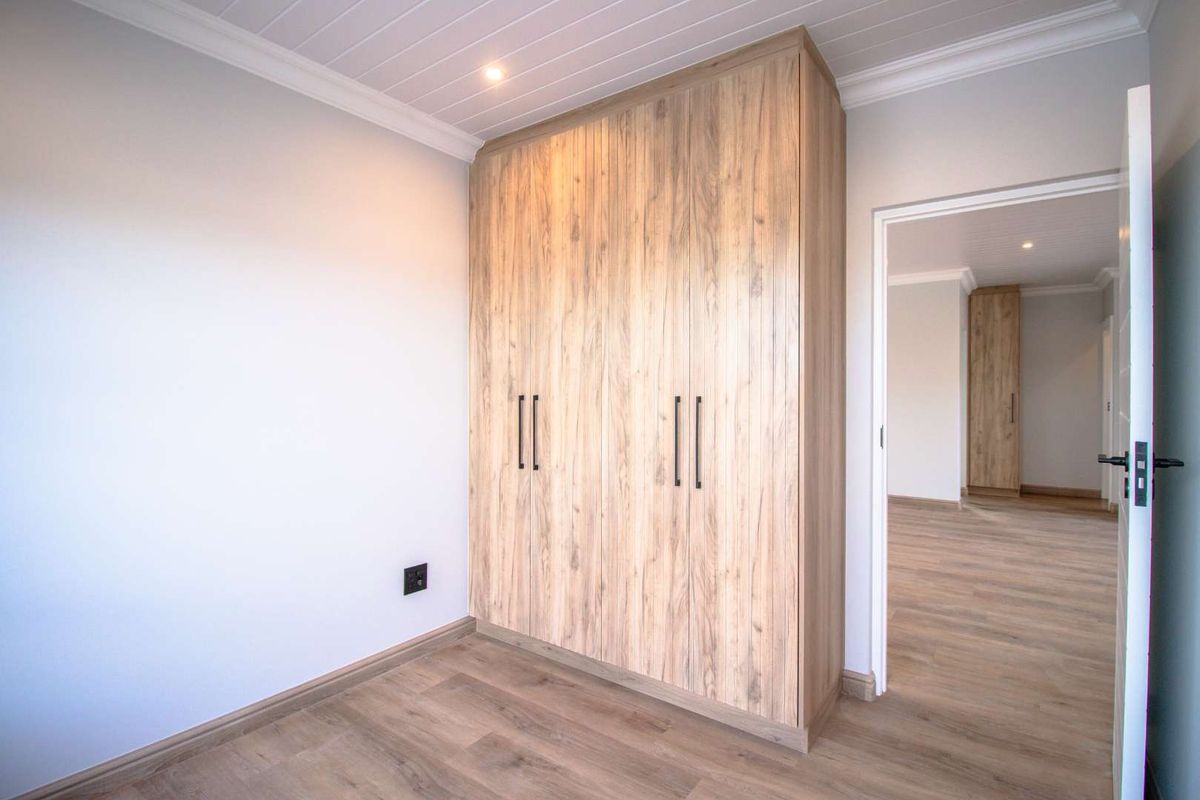 A bright bedroom featuring modern wood-grain built-in cupboards, light timber-look flooring, and recessed ceiling lighting.