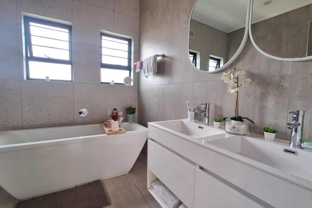 Modern bathroom featuring a sleek freestanding bathtub, a contemporary double vanity with chrome fixtures, and neutral floor-to-ceiling wall tiles.