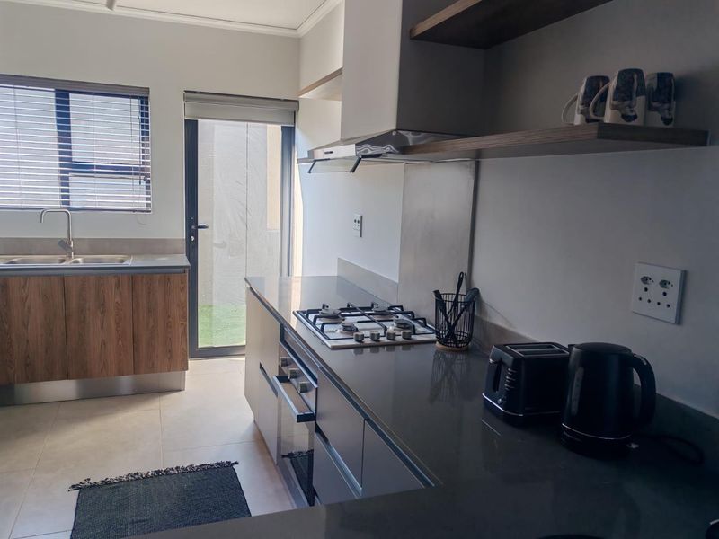 Modern kitchen featuring stone countertops, gas hob, built-in oven, extractor fan, and direct access to an outdoor area through a sliding glass door.